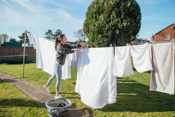 Woman hanging freshly washed sheets on a clothesline in a sunny backyard for wrinkle-free drying.